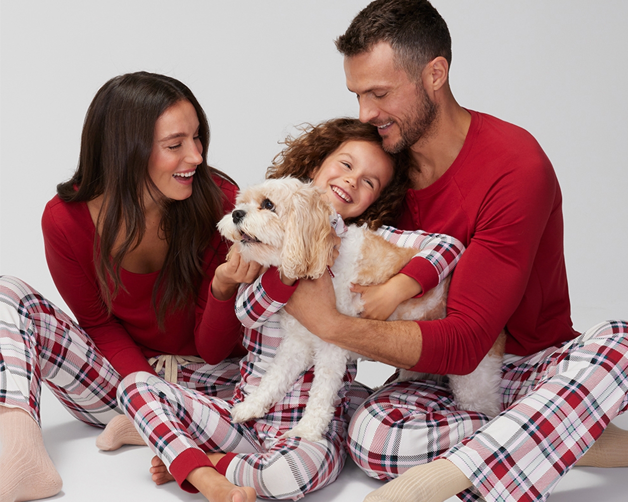 Soma<sup class=st-superscript>®</sup> models wearing matching red and white plaid family pajamas + dog wearing matching pet bandana.