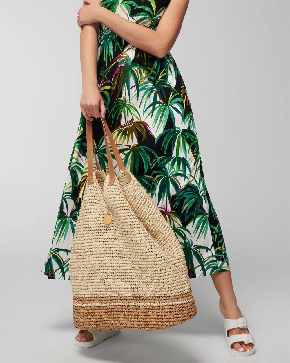 Soma<sup class=st-superscript>®</sup> model wearing a white, black, and green palm print bra dress, white slide sandals, and a tan oversized beach bag.