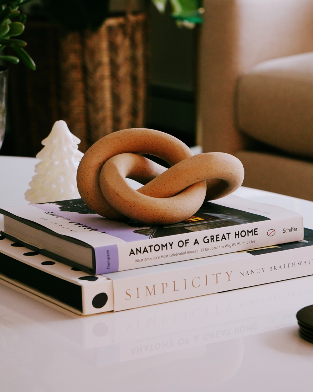 Two coffee table books stacked on each other with a brown decorative chain on top and white tree figurine.