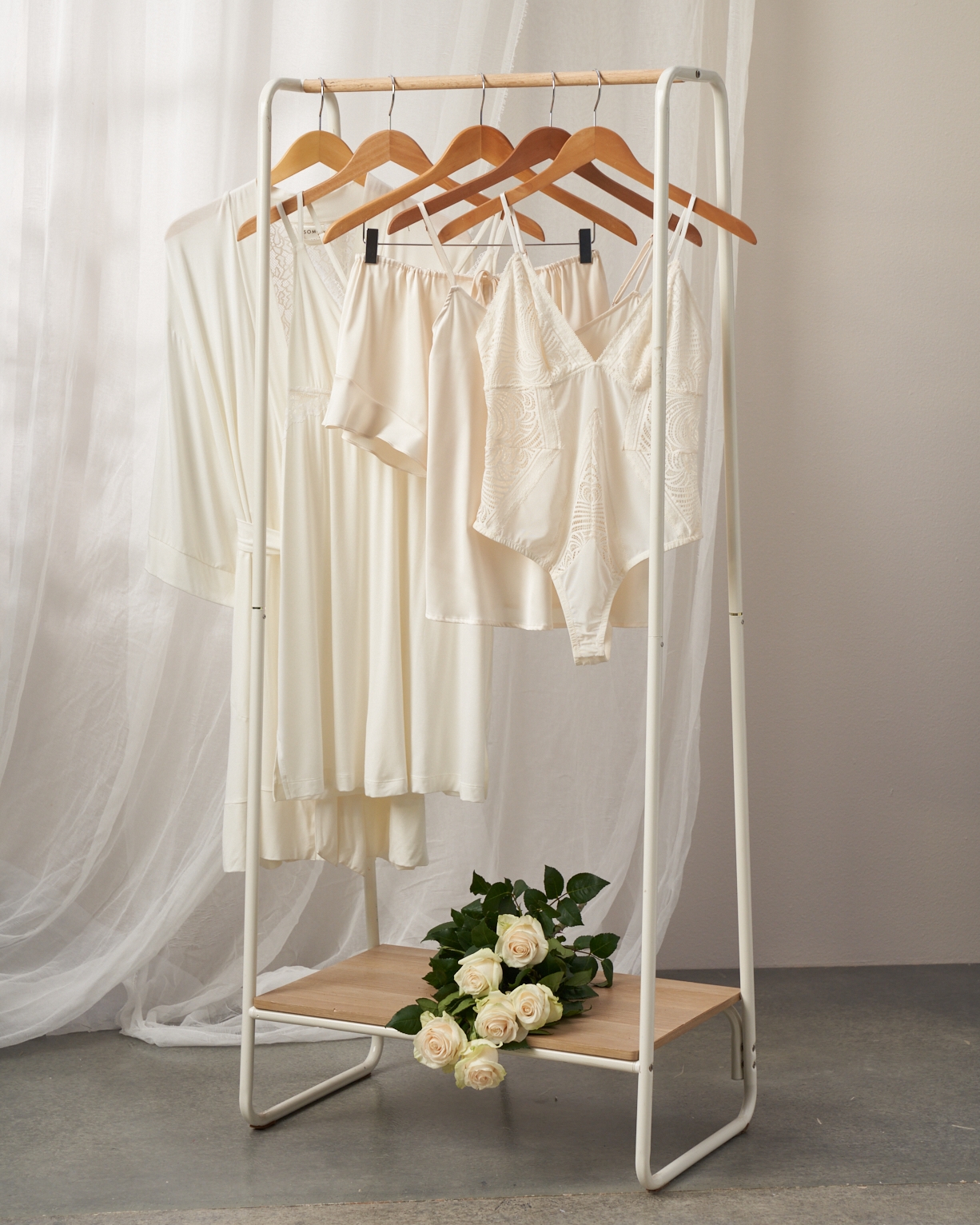 Soma<sup class=st-superscript>®</sup> women’s ivory bridal lingerie hanging on a rack and white roses in a bundle on the bottom shelf.