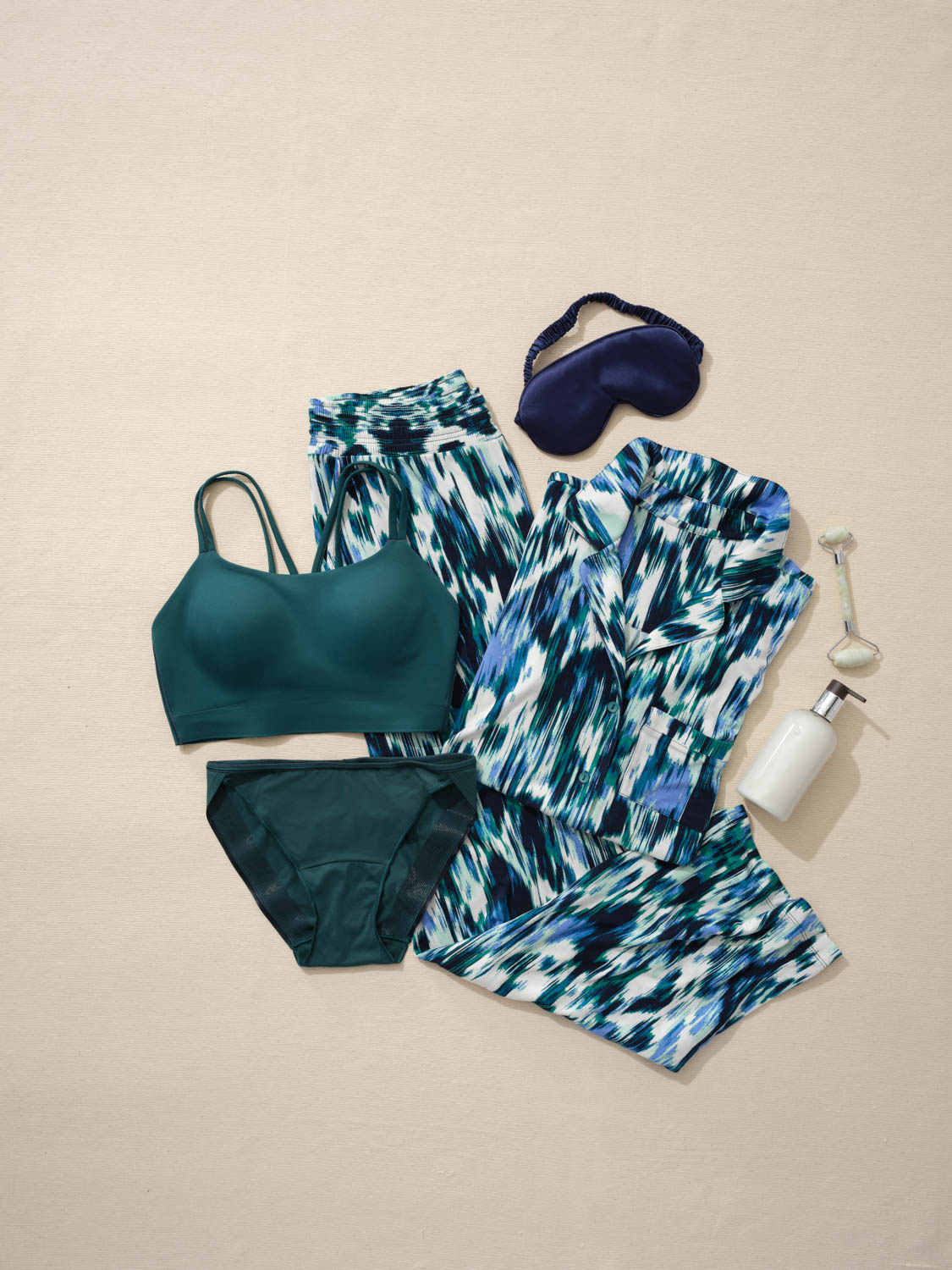 Soma<sup class=st-superscript>®</sup> laydown of green bralette and matching panties, matching multi-colored printed pajamas, eye mask, jade roller, and lotion bottle.