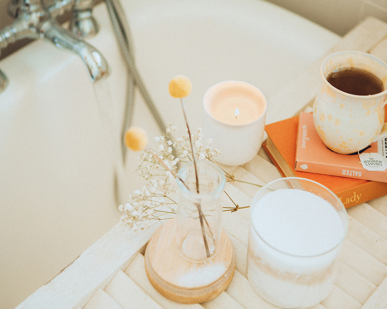 Bathtub with candles, flower in vase, and mug of tea sitting on two books.
