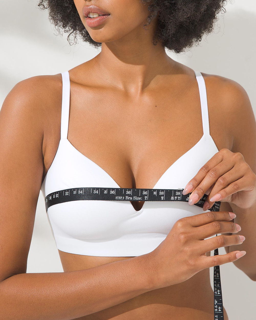 Soma<sup class=st-superscript>®</sup> model wearing a white wireless bra wrapping a black measuring tape around her bust.