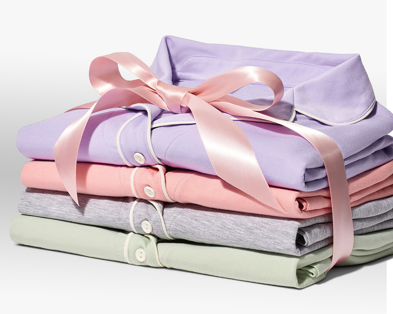 Stack of purple, pink, grey, and green pajama button-up tops wrapped in a pink satin bow.