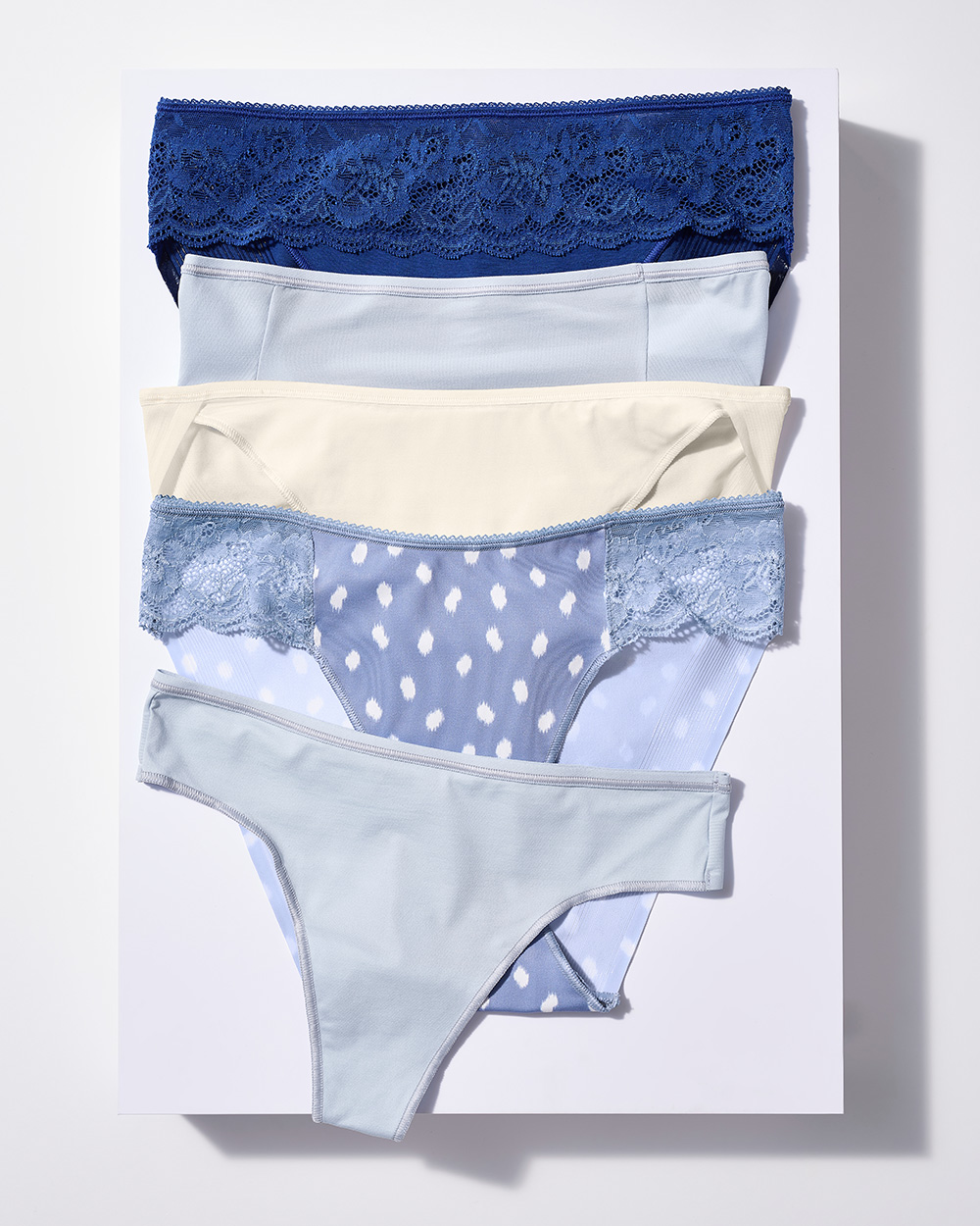 Soma<sup class=st-superscript>®</sup> laydown of white, light blue, and dark blue panties in various silhouettes, cascading in a vertical row.