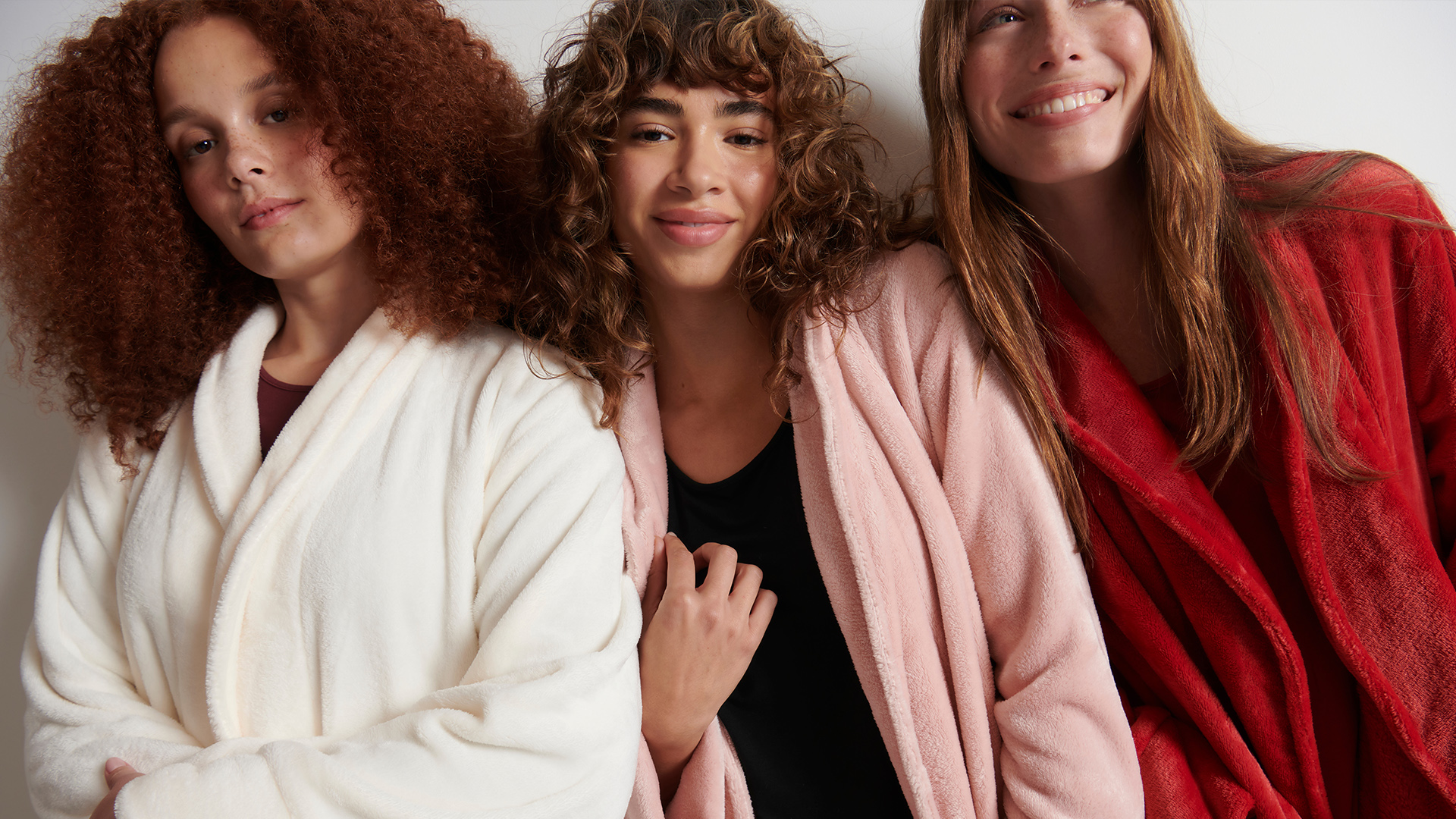 Soma<sup class=st-superscript>®</sup> models huddled together wearing white, light pink, and red plush robes.