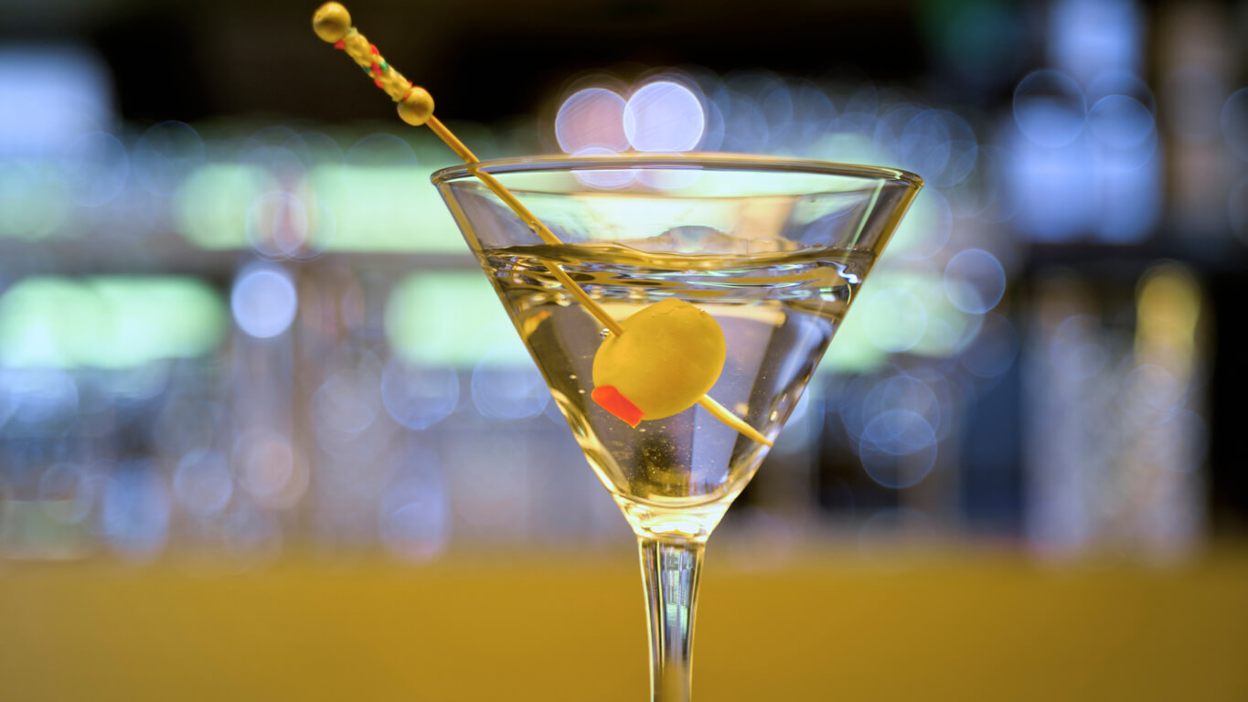 Close-up of martini cocktail with olive on table in bar.