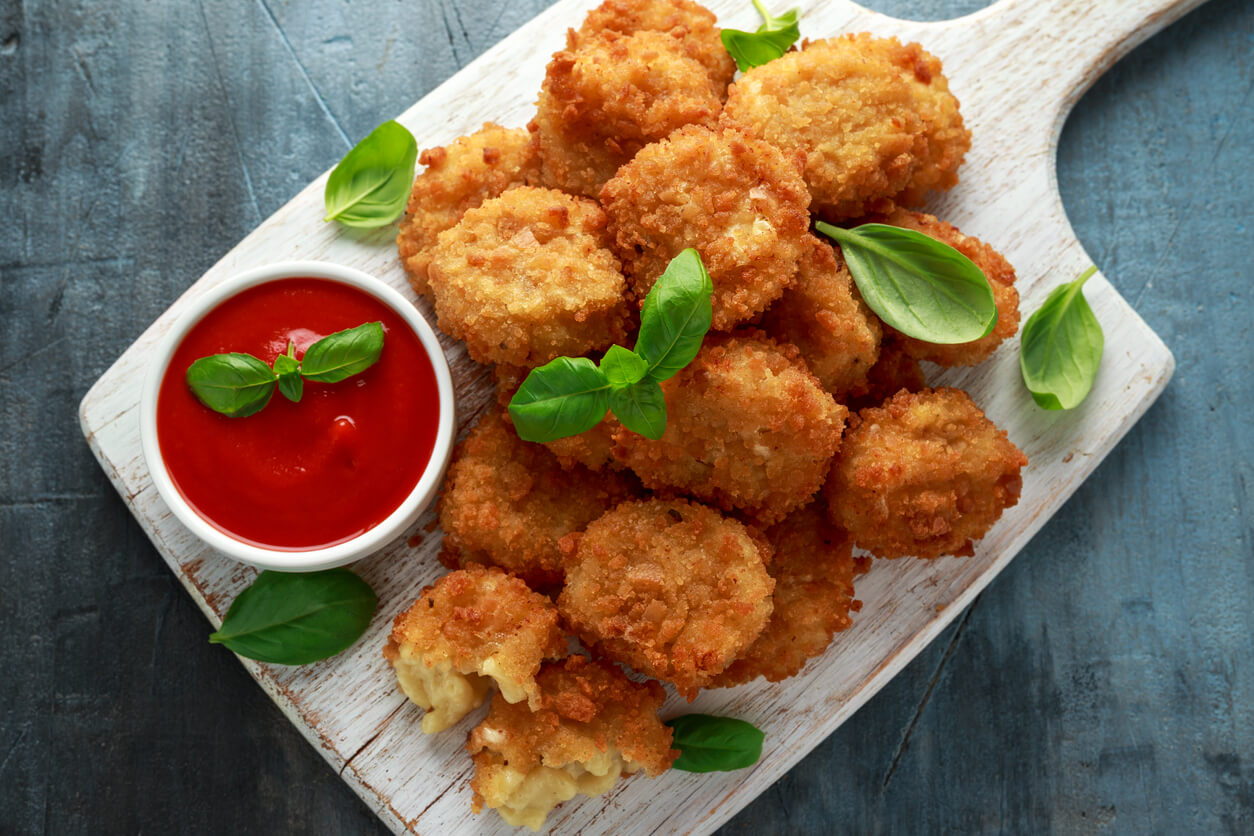 Fried Mac, macaroni and Cheese Bites in breadcrumbs with ketchup sauce on white wooden board