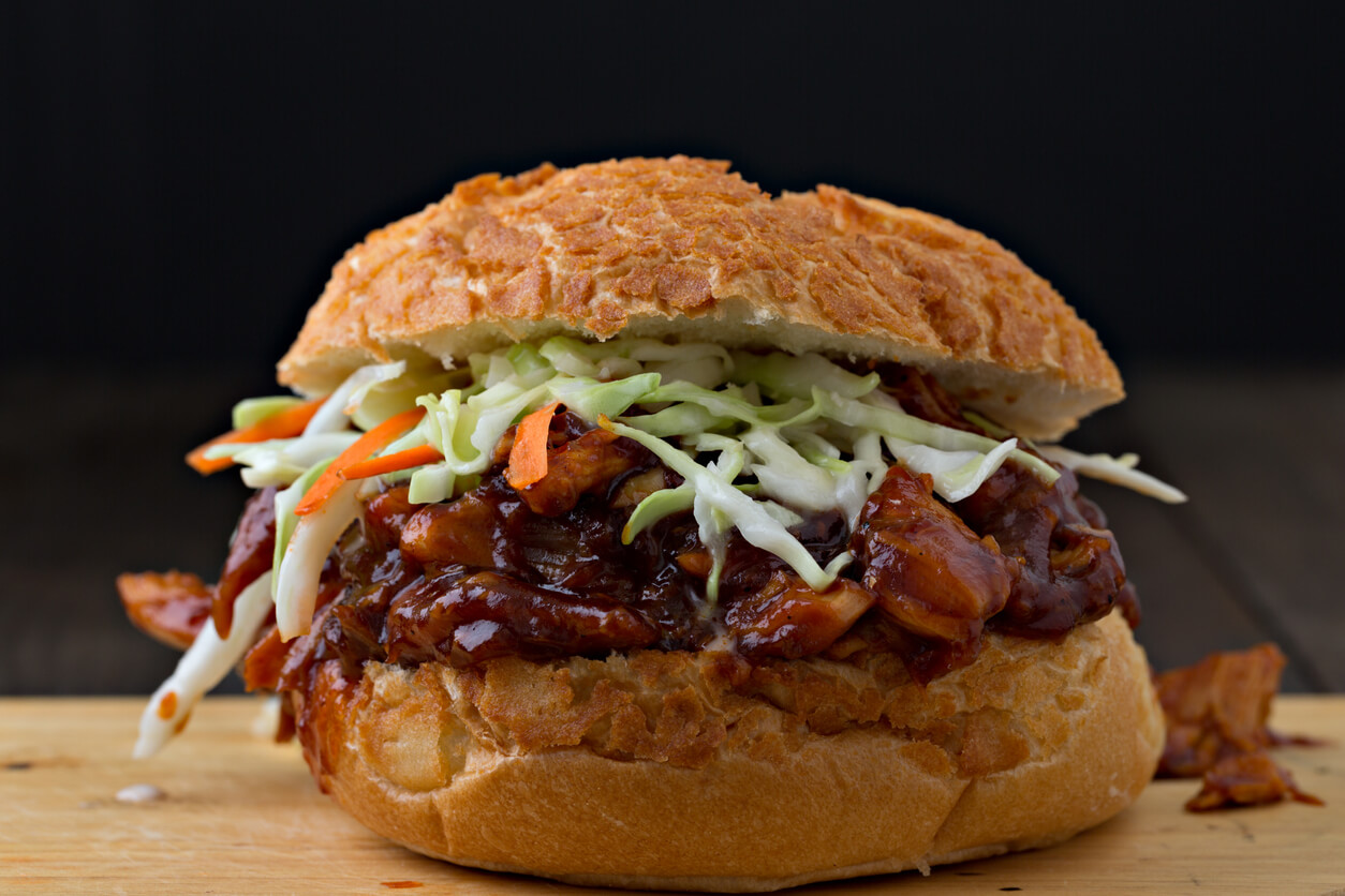 An extreme close up horizontal photograph of a barbecued, pulled chicken sandwich topped with freshly made crisp coleslaw in a dutch crust bun.