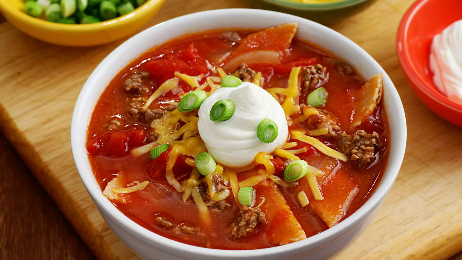 A bowl of keto taco soup with sour cream on a wooden serving board.