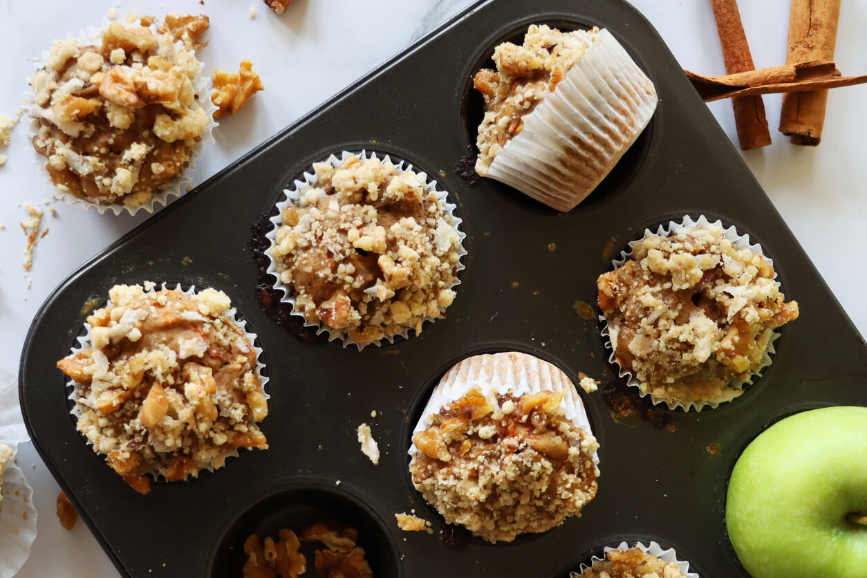 muffin baking tray containing homemade apple muffins, with streusel crumble topping.
