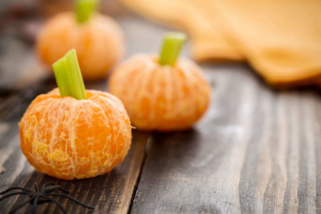 Tangerine jack o'lanterns made of tangerines and celery stick with spider decoration. These healthy halloween are fun food for kids on rustic wood table.