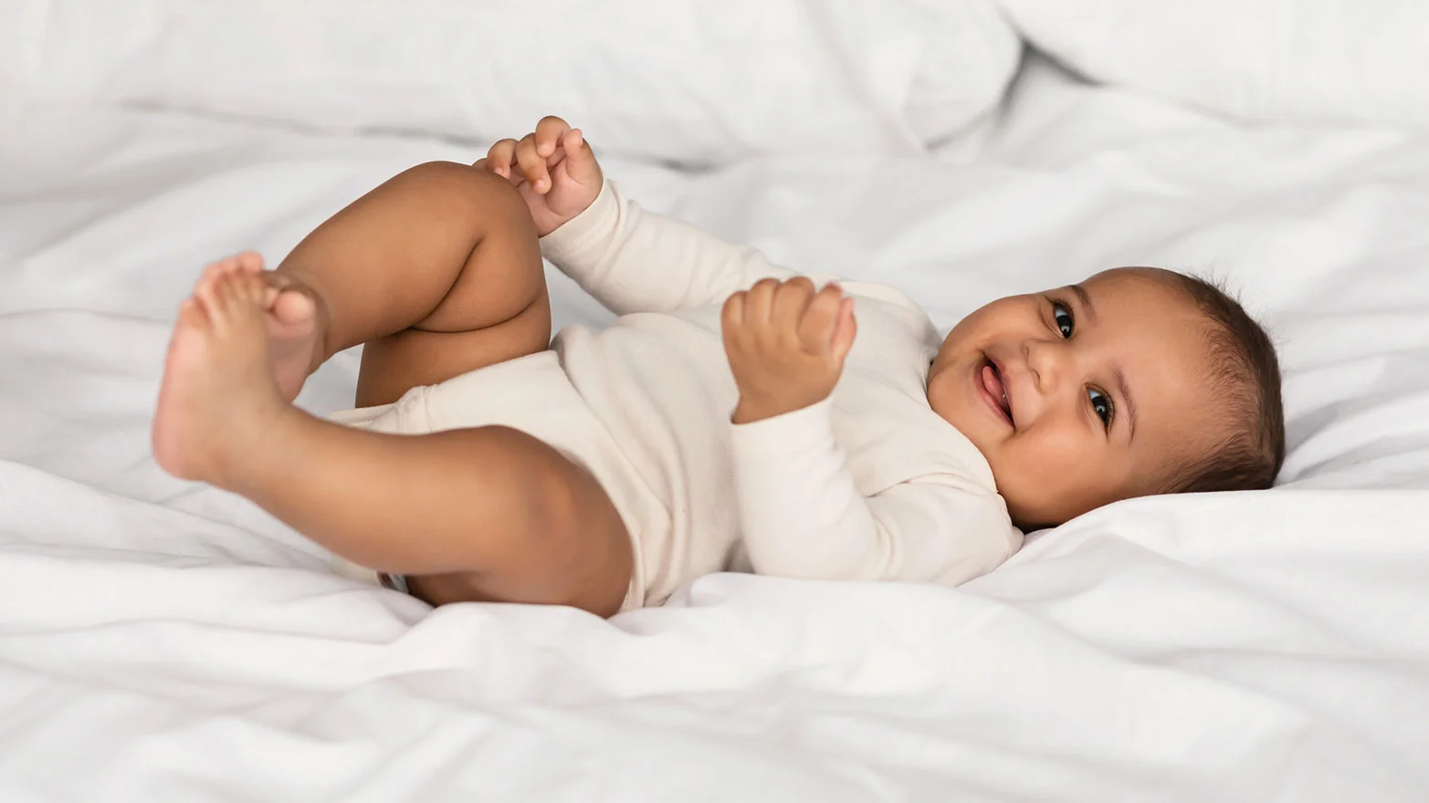 A stock photo of a laughing baby wearing a beige bodysuit onesie.