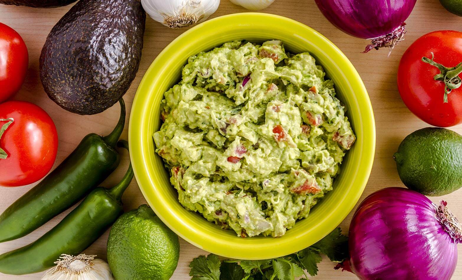 a bowl of chunky guacamole dip surrounded by fresh vegetables