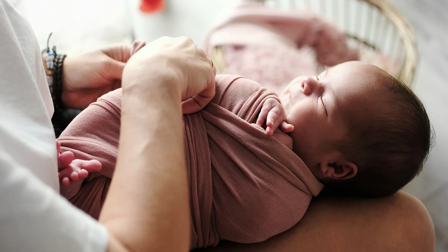 A stock photo of a baby in a specialized pink swaddle blanket.