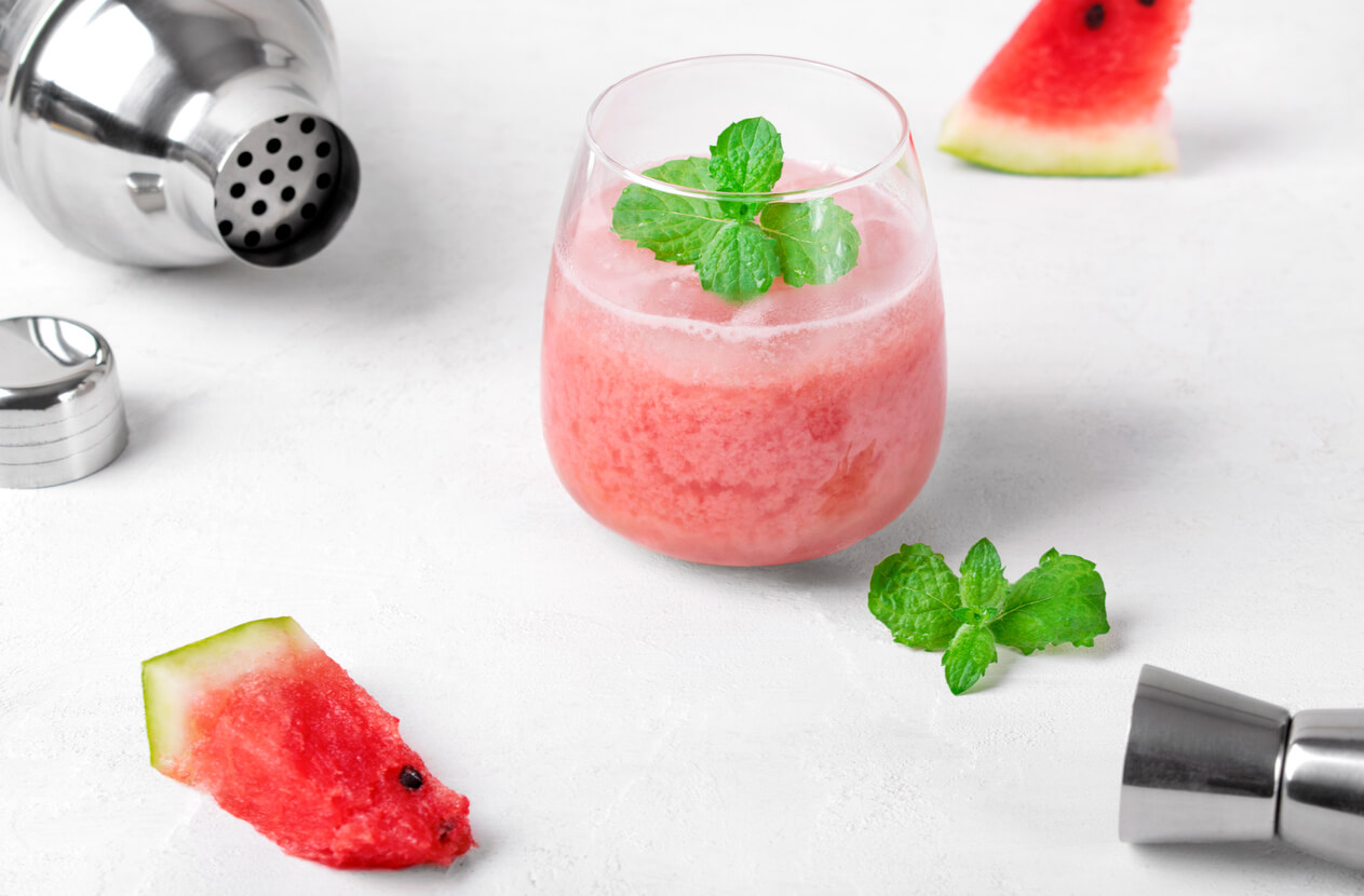 Watermelon crush with coconut milk, pineapple juice and mint in the drinking glass on the white table. Refreshing summer drink.