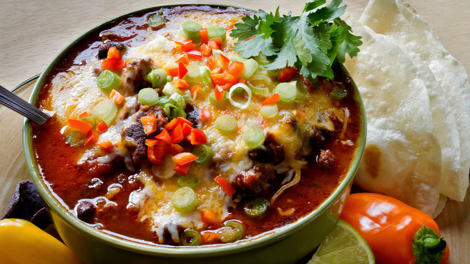 A colorful bowl of cheesy enchilada soup served with tortillas.