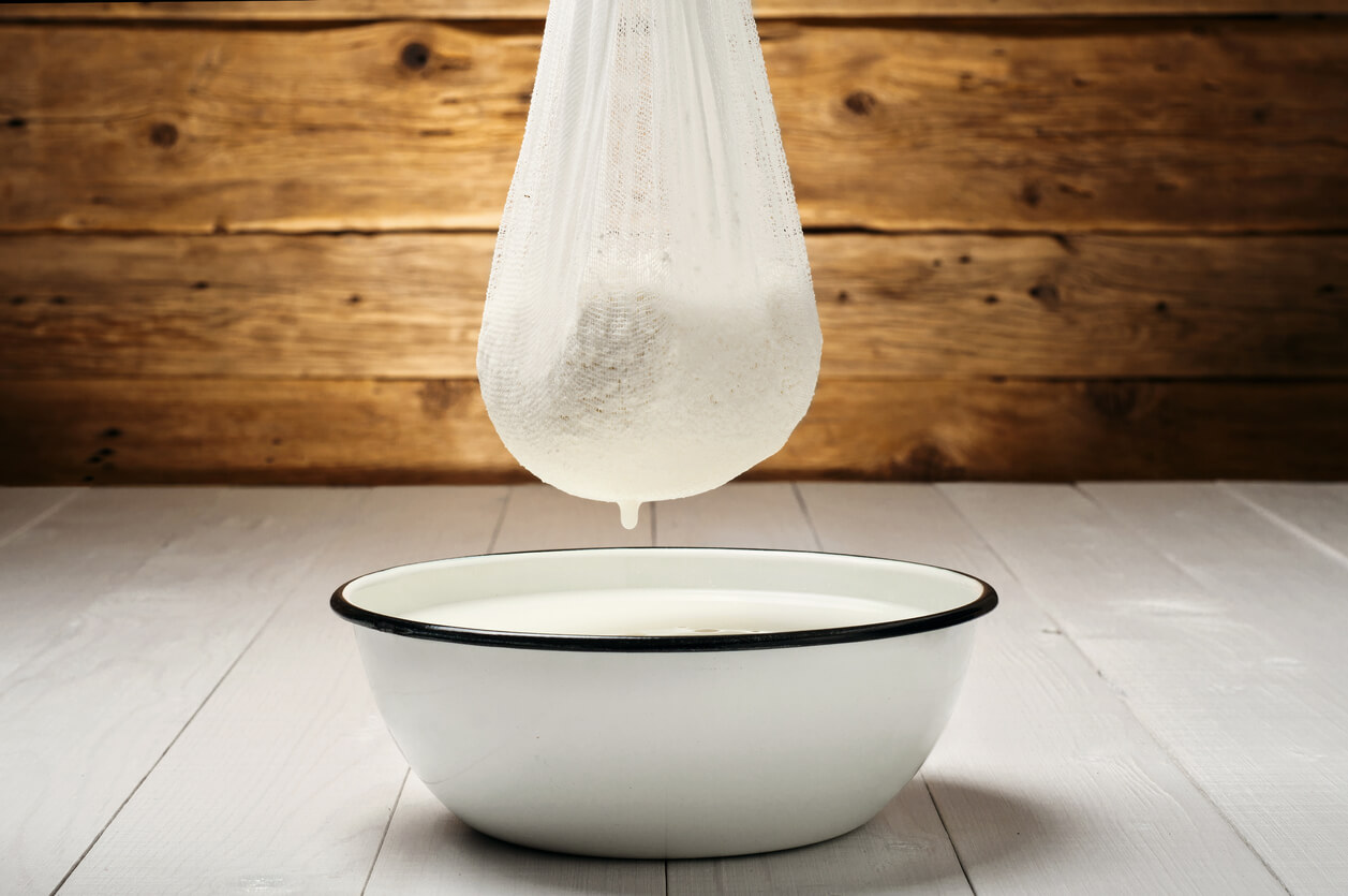 Cottage cheese in cheesecloth flows into the emulsion white dish on a white wooden table