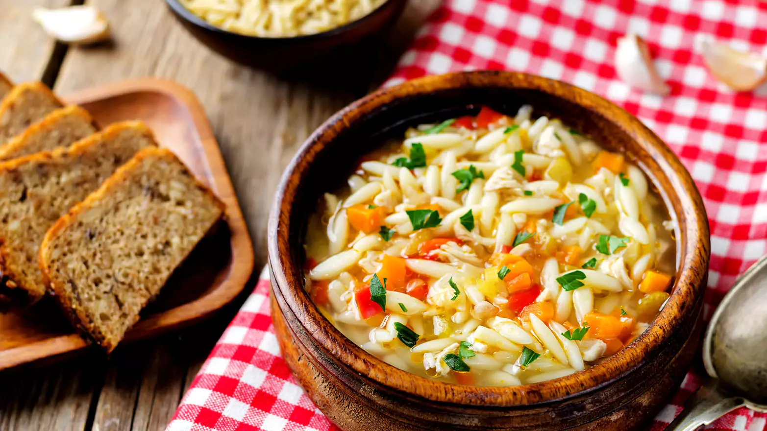 A bowl of hearty orzo soup served with bread.