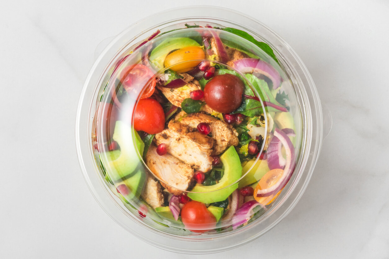 Plastic package with healthy chicken salad with avocado , tomatoes and pomegranate to take away