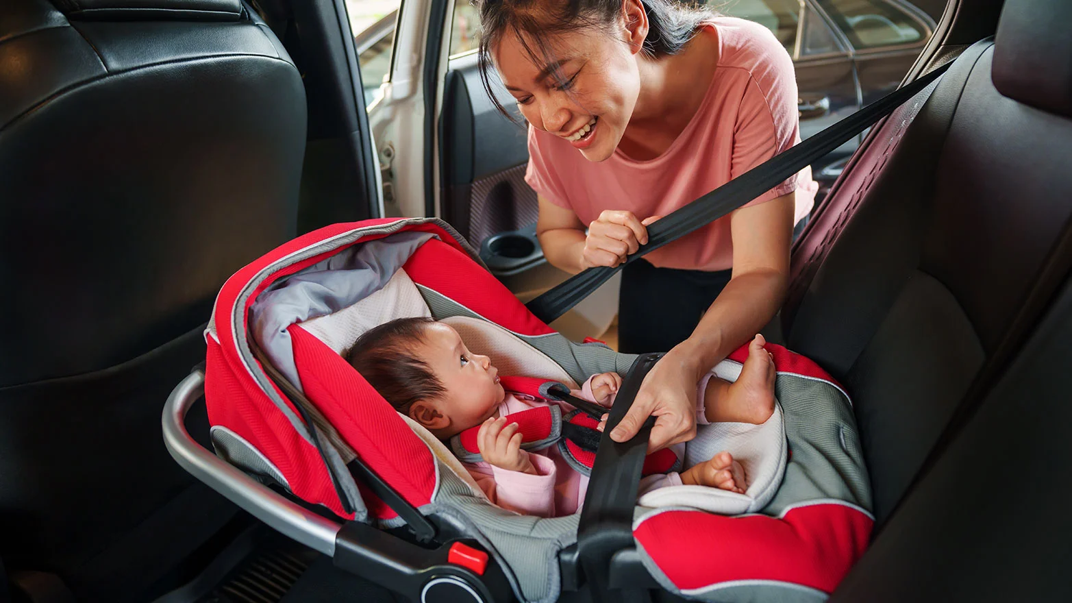 A stock photo of a mother buckling a baby into a car seat.