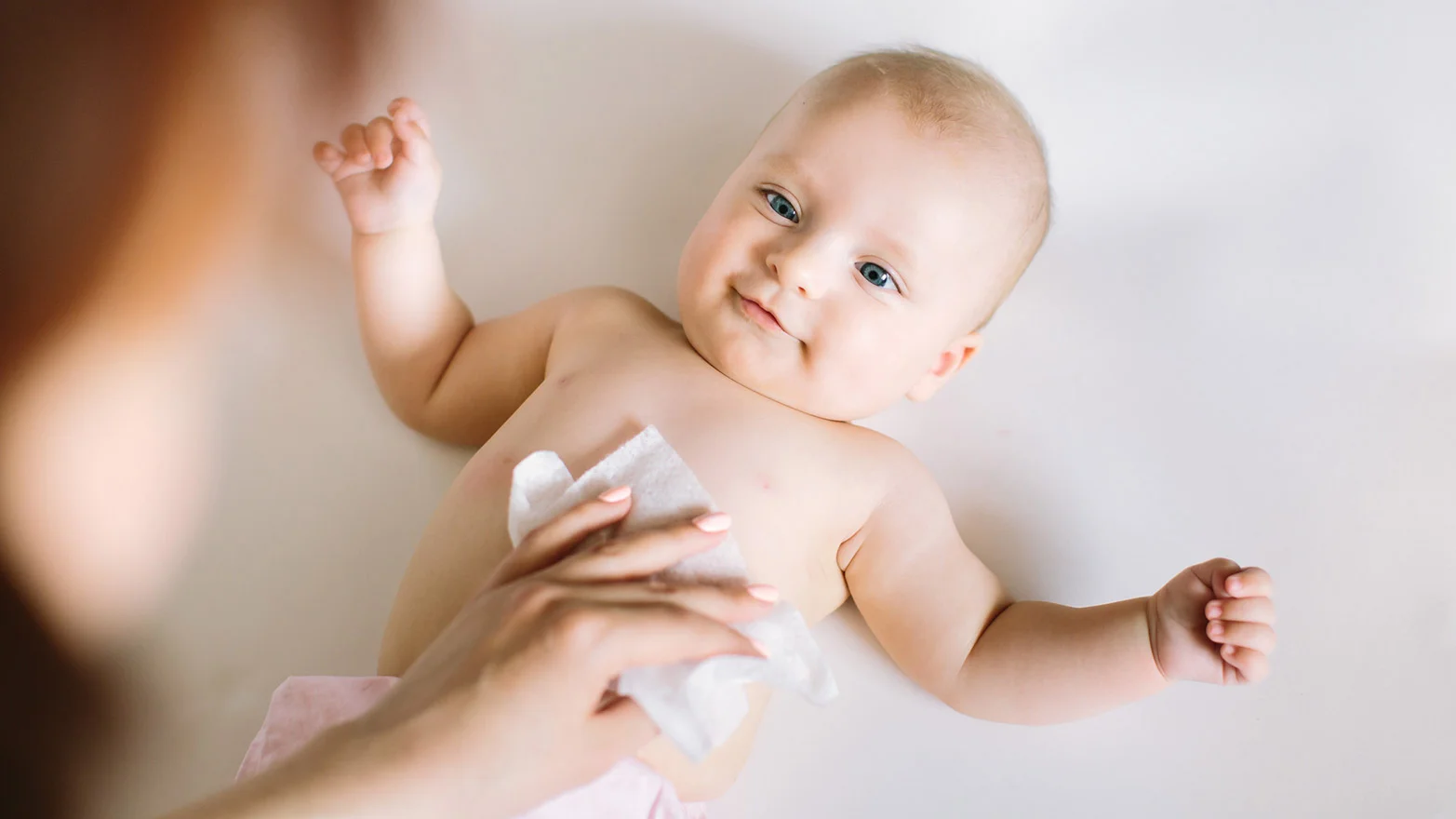 A stock photo of a person using a baby wipe on a baby’s chest.