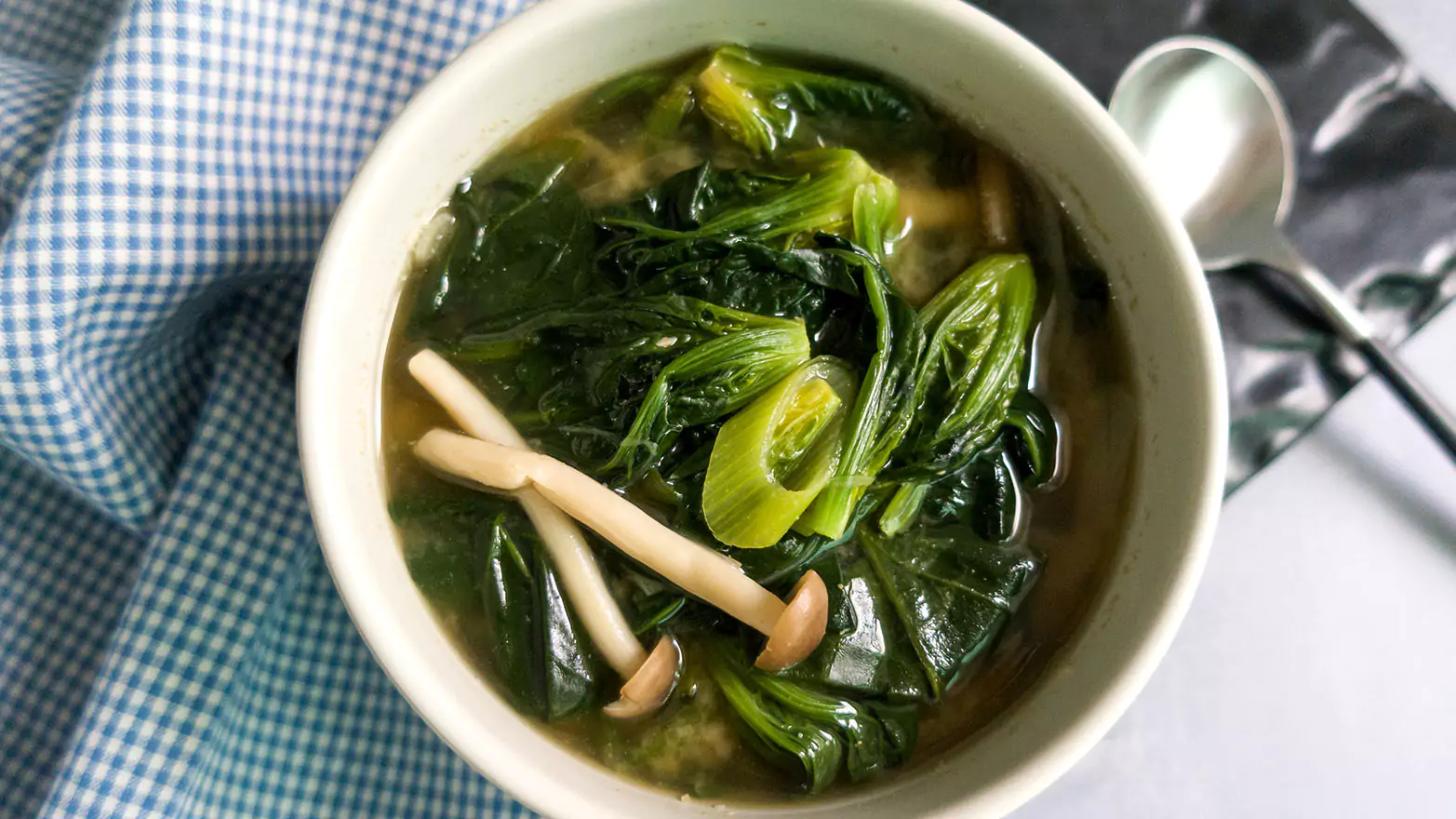 A bowl of bok choy soup on a checkered tablecloth.
