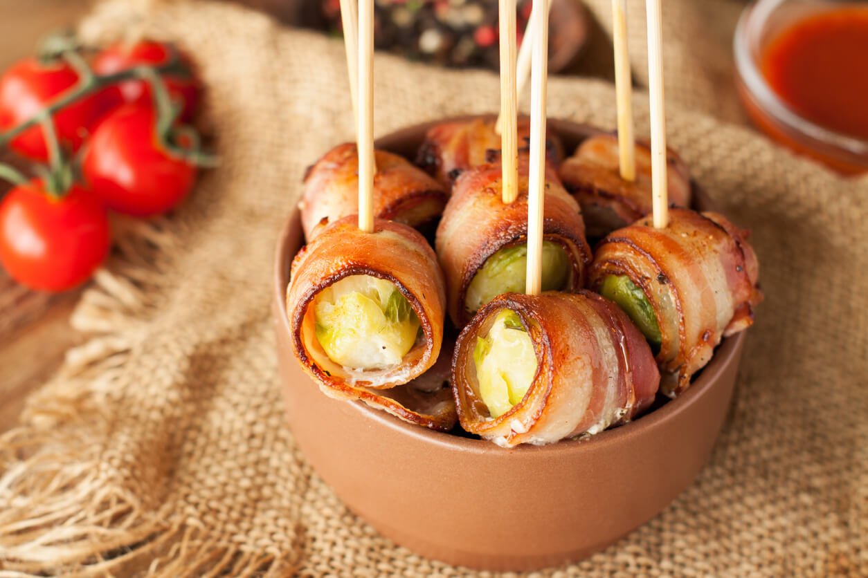 Bacon wrapped brussels sprouts served with cherry tomatoes in ceramic bowl.