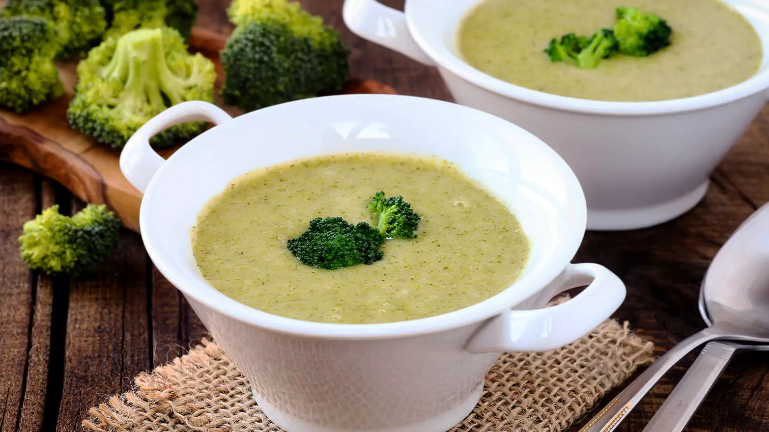 Two servings of broccoli soup with fresh chopped broccoli in the background.