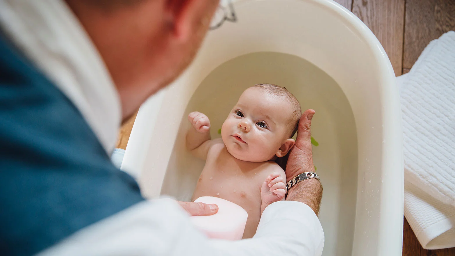 A stock photo of a parent bathing their baby in an infant bathtub.
