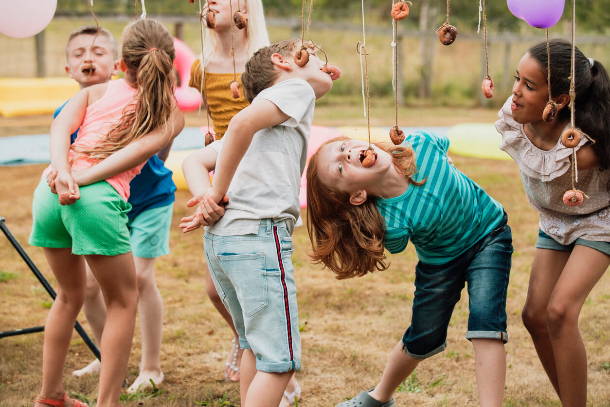 A close-up shot of a group of young children playing a party game, they are eating donuts of a string with their hands behind their back.