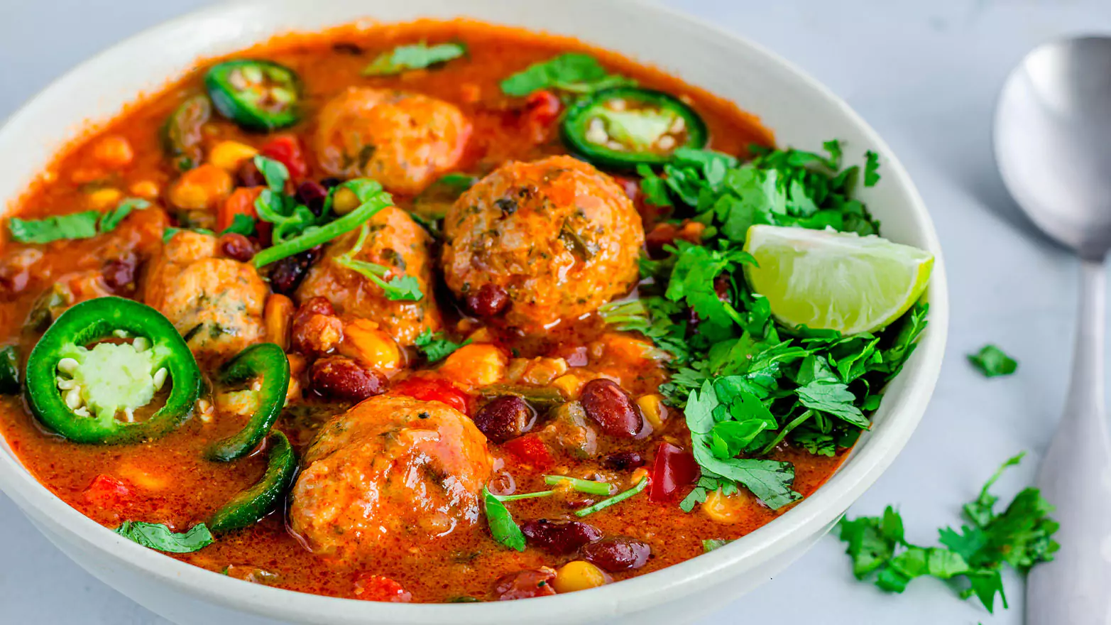 A bowl of Mexican meatball soup with lots of jalapeno slices.