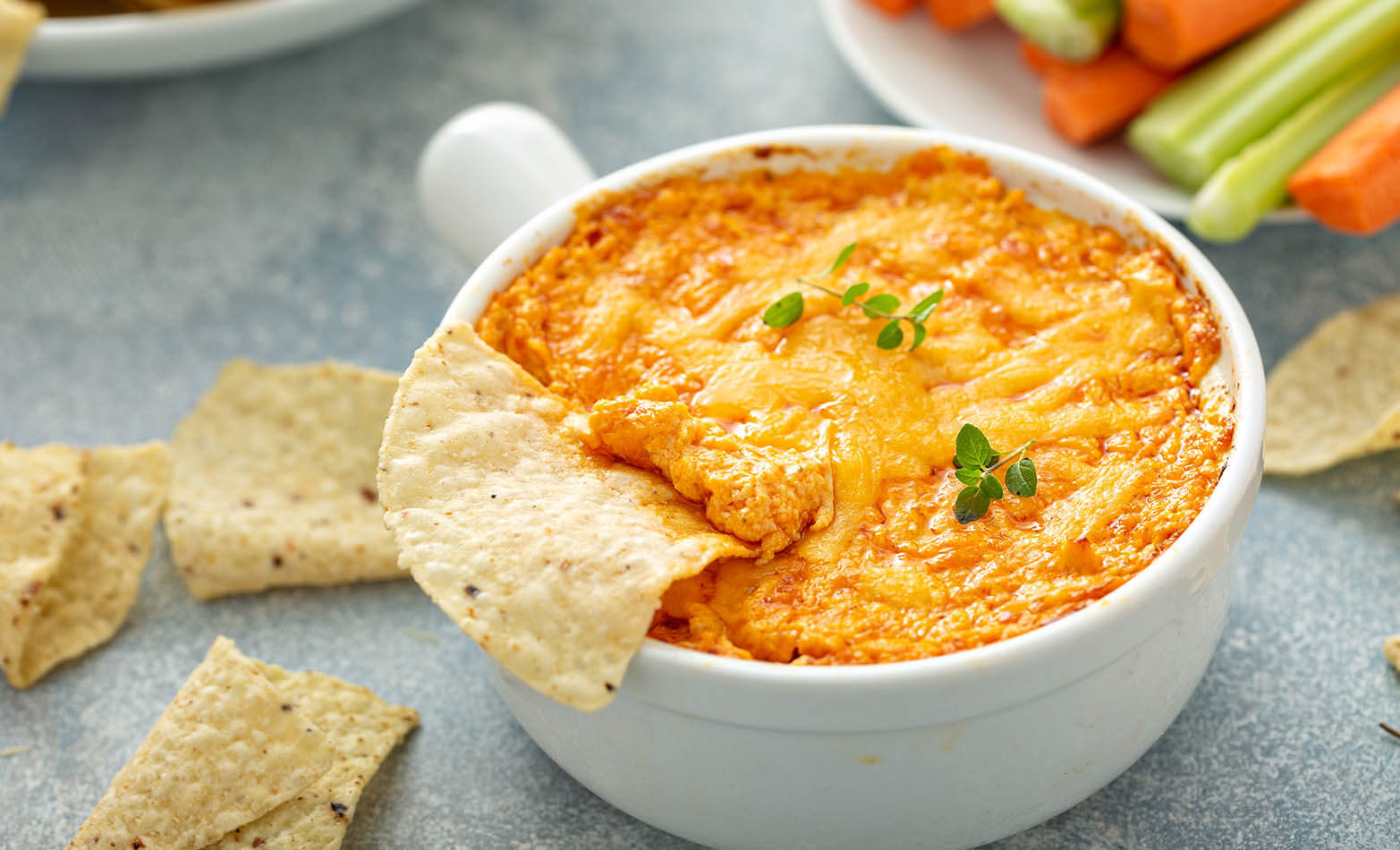 a bowl of buffalo chicken dip served with chips, carrots, and celery sticks