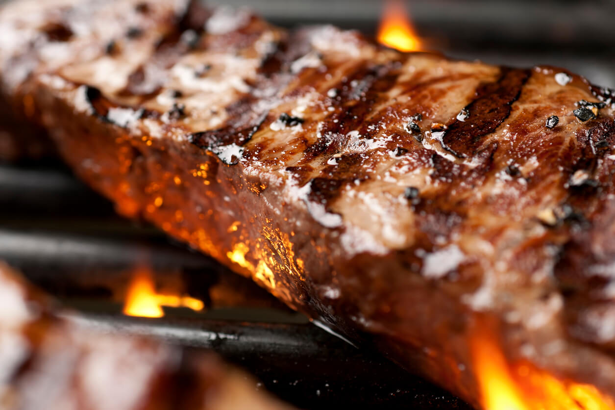 Close up of NY strip steak cooking on the grill.