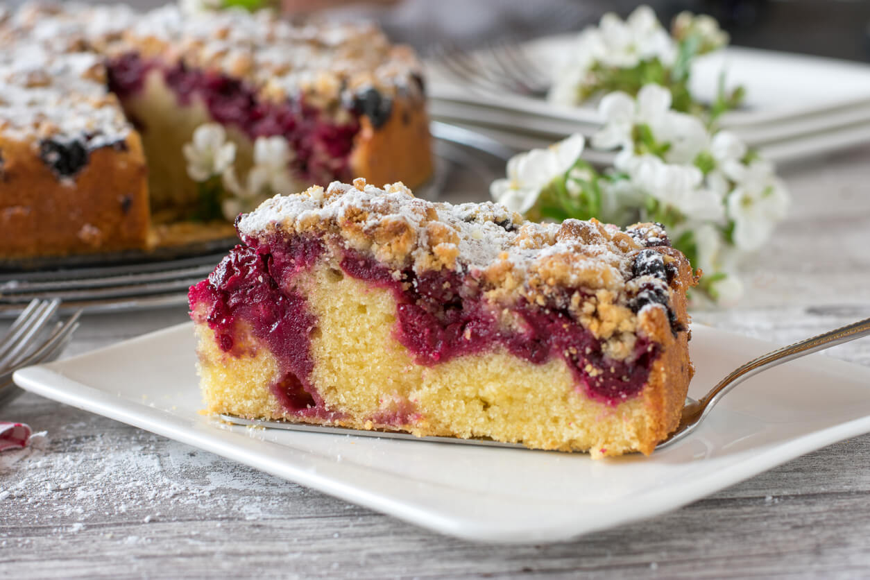 A Piece of Cherry crumble cake on a plate on white wooden table.