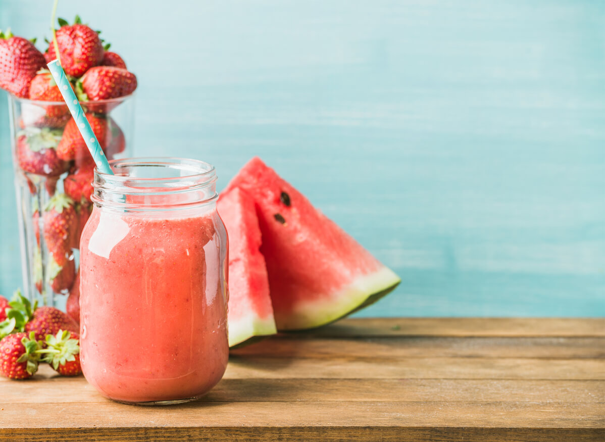 Freshly blended red fruit smoothie in glass jar with straw