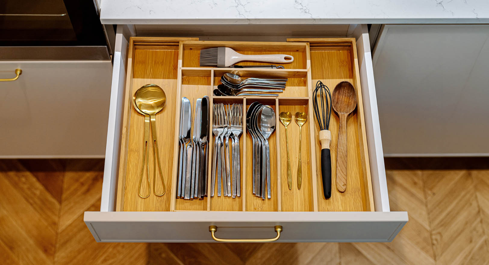 A photo of an open kitchen drawer, revealing an assortment of utensils inside a wooden drawer organizer.