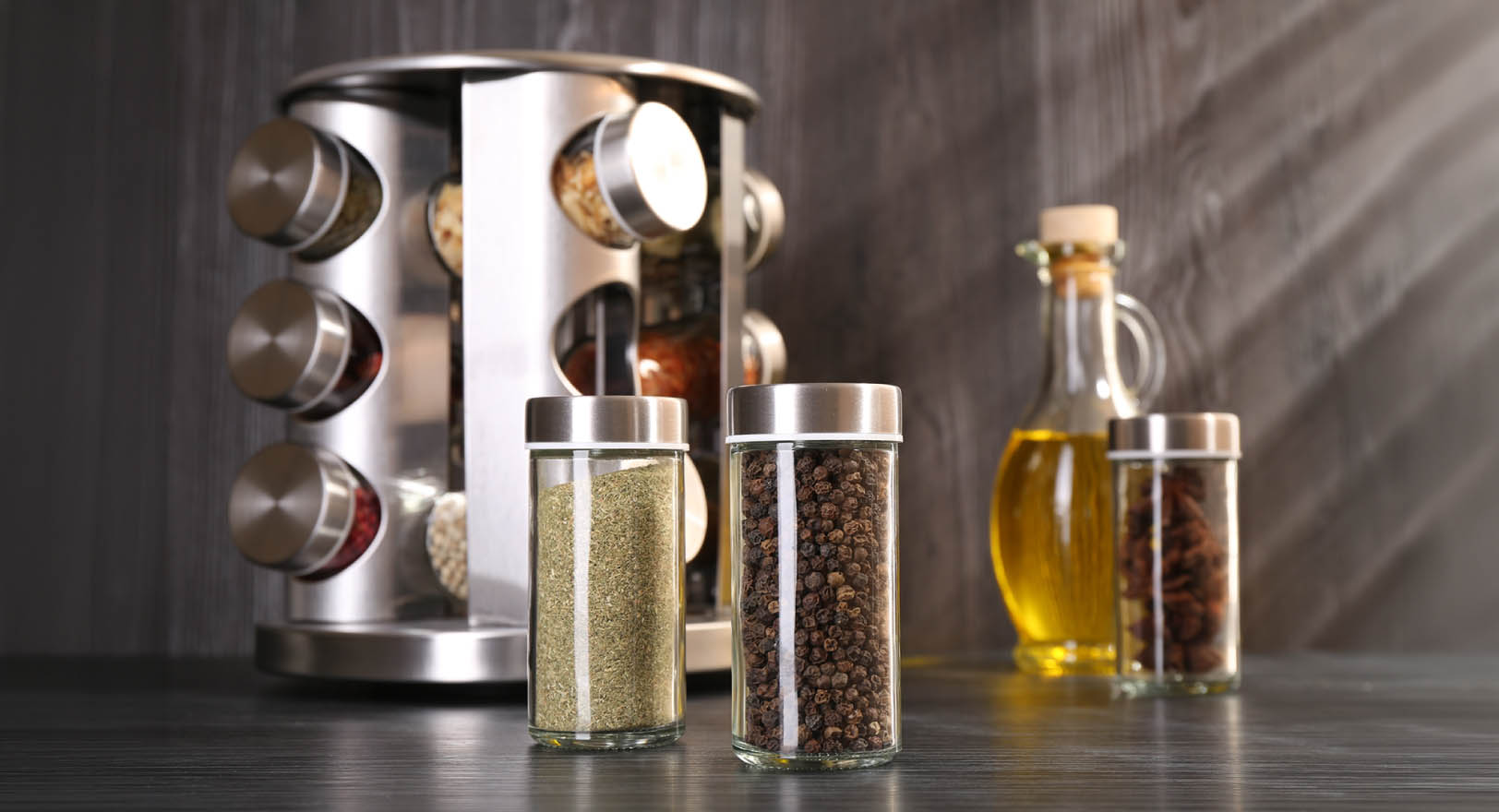 A photo of a metal spice rack on a sleek kitchen counter next to a bottle of olive oil.