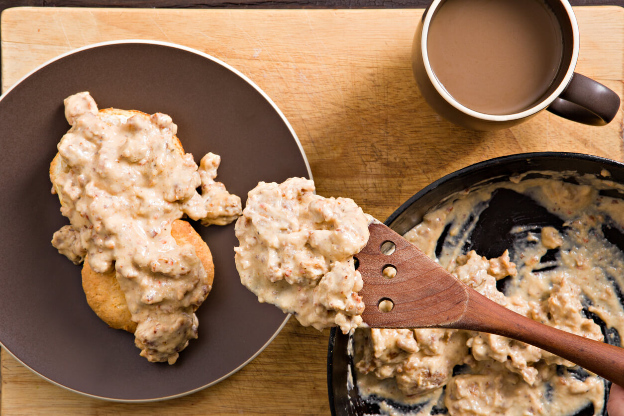 An overhead close up shot of a hand scooping up some sausage and gravy from an old cast iron pan.