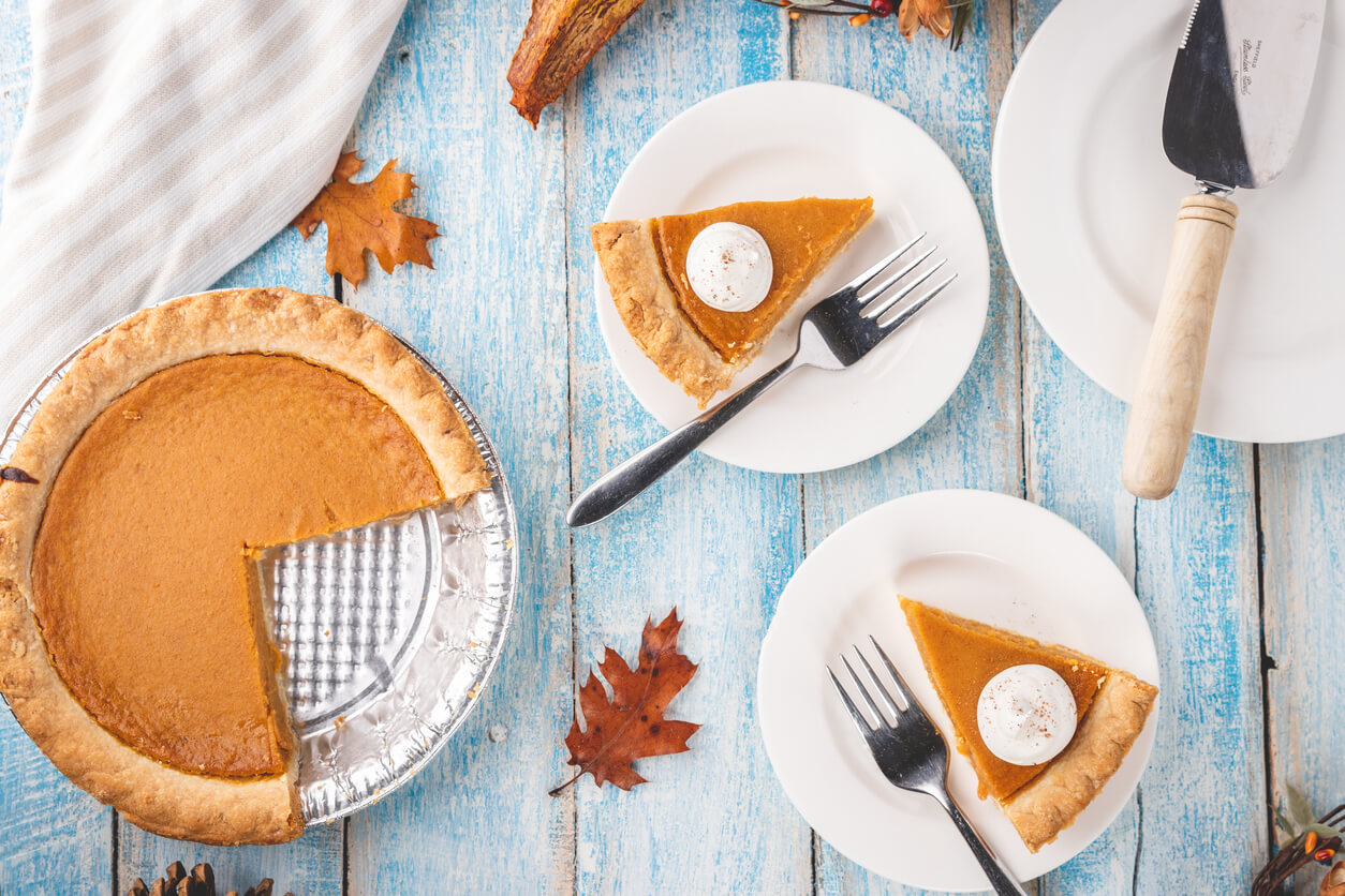 Overhead flat lay shot of a pumpkin pie in a tin with two slices of pumpkin pie on plates with forks.