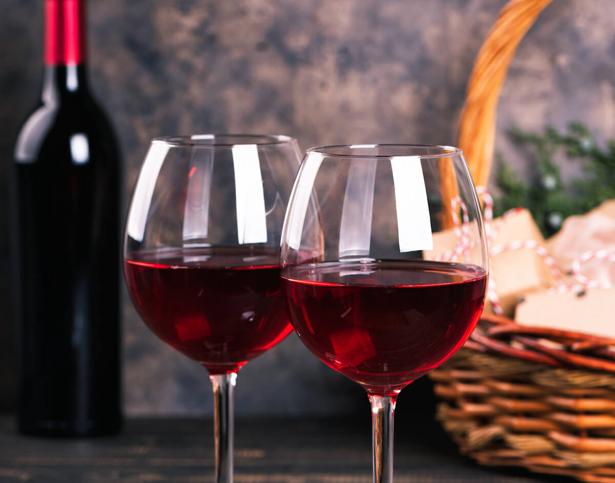 Bottles of red wine and Christmas basket. Mulled wine with gift boxes, cookies and fir-tree ornaments.