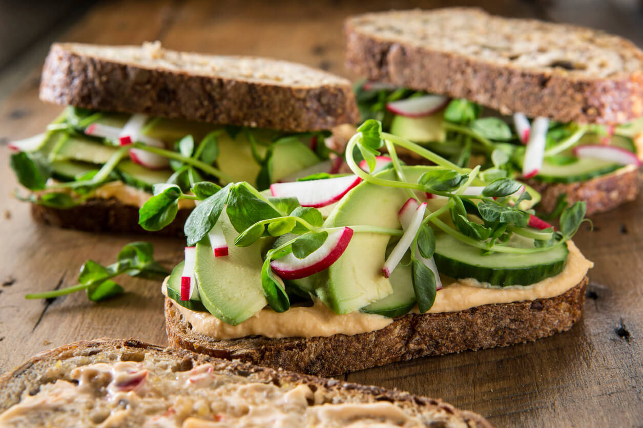 Three sandwich's on multigrain bread with red pepper hummus ,cucumber ,pea shoots ,avocado and radish's.