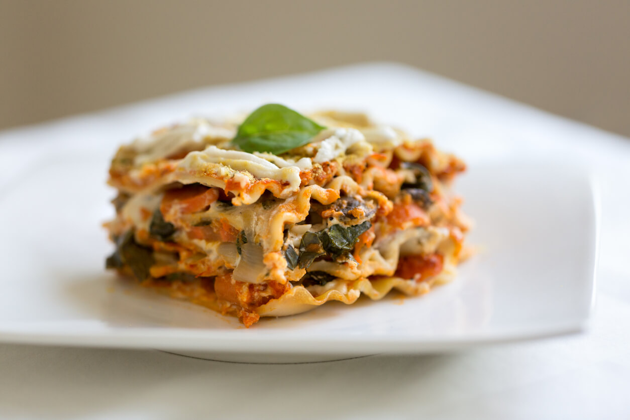 Vegan lasagna with vegetables, tomato sauce, cashew sauce and garnished with fresh basil and nutritional yeast.