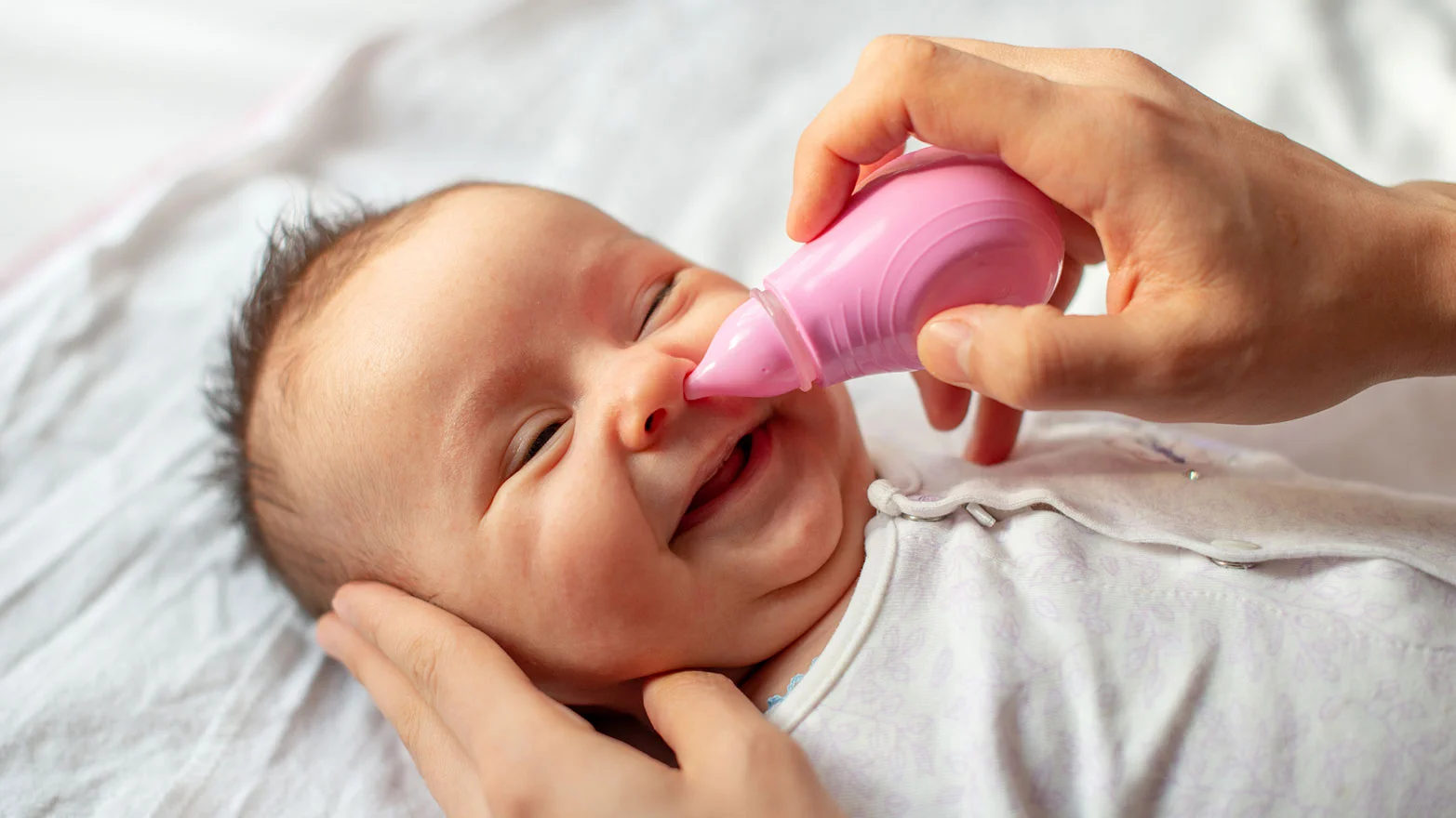 A stock photo of a baby with a pink nasal aspirator.