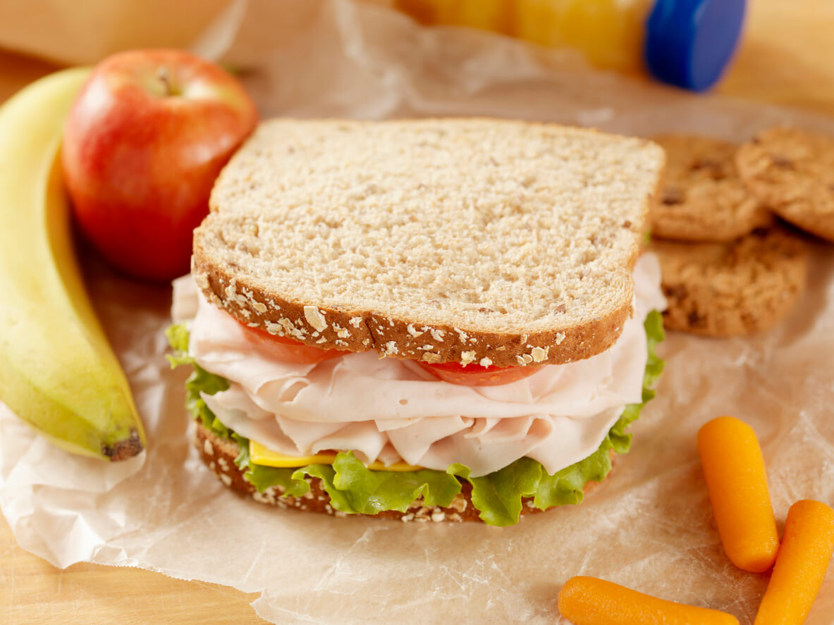 Healthy Packed Lunch with a Turkey, lettuce, Tomato and cheese Sandwich with Fresh fruit, Orange Juice, Baby Carrots and Cookies