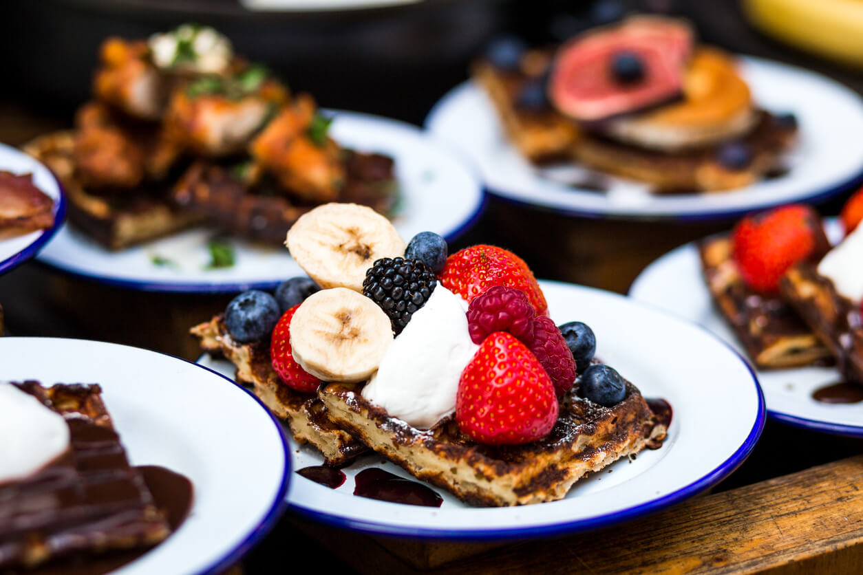 Close up color image depicting plates of fresh sweet waffles topped with strawberries, blackberries, ice cream and fresh figs. These desserts are on display and for sale at a food market in London, UK. Selective focus on one of the desserts in the foreground, while the others are pleasantly defocused, allowing room for copy space.
