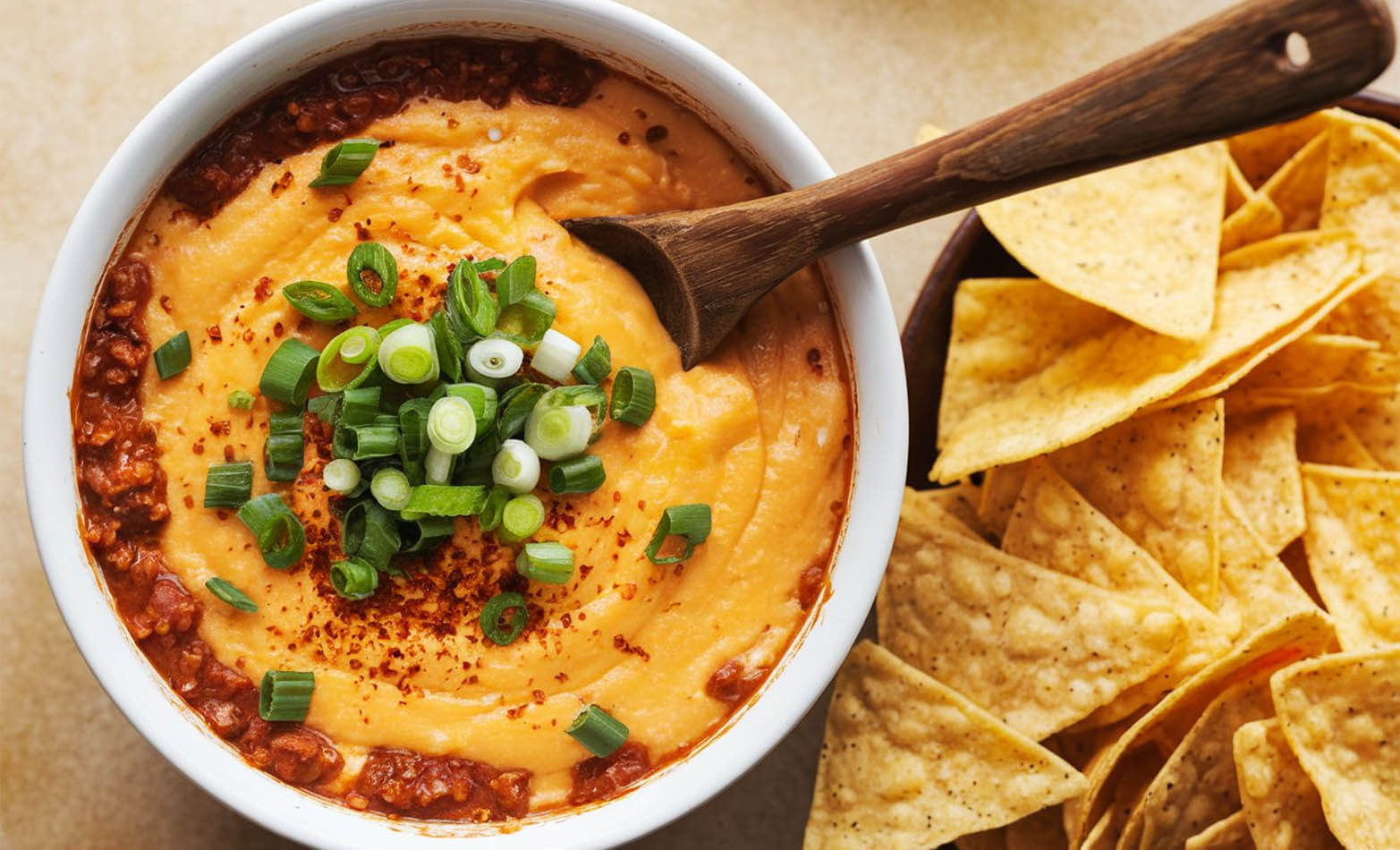 a bowl of queso dip with a wooden serving spoon and a side of tortilla chips