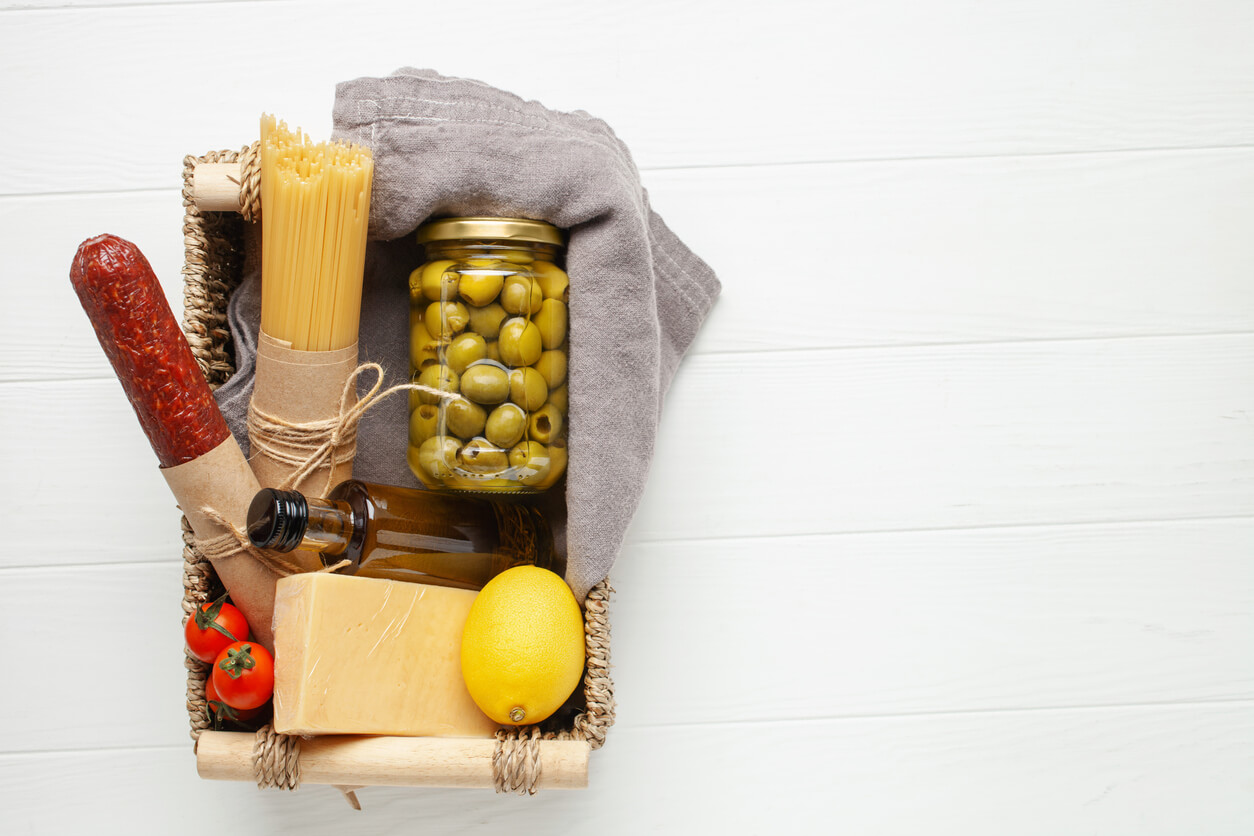 Spaghetti, tomatoes, olives, olive oil, cheese, lemon and salame. Products food in jars in a gift basket.
