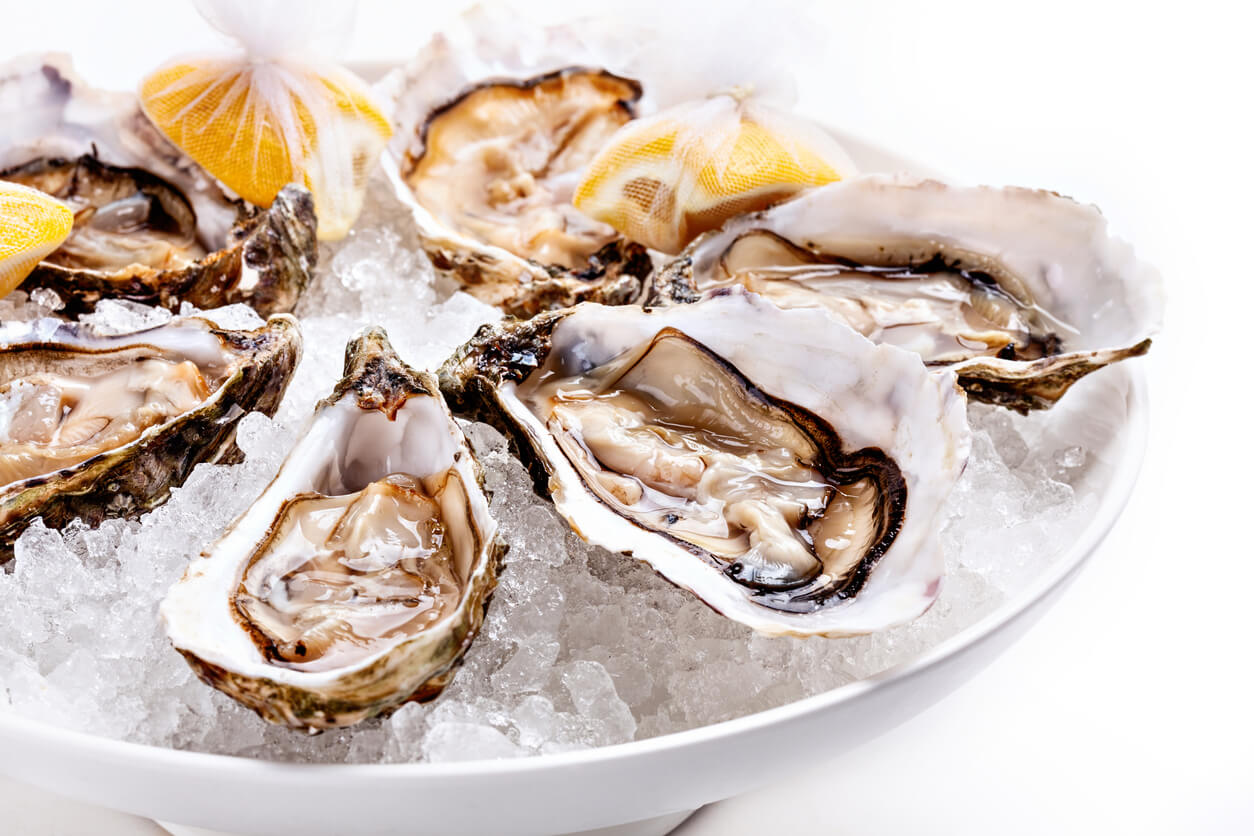 Half dozen fresh oysters are served with lemon in bowl with plenty of ice.
