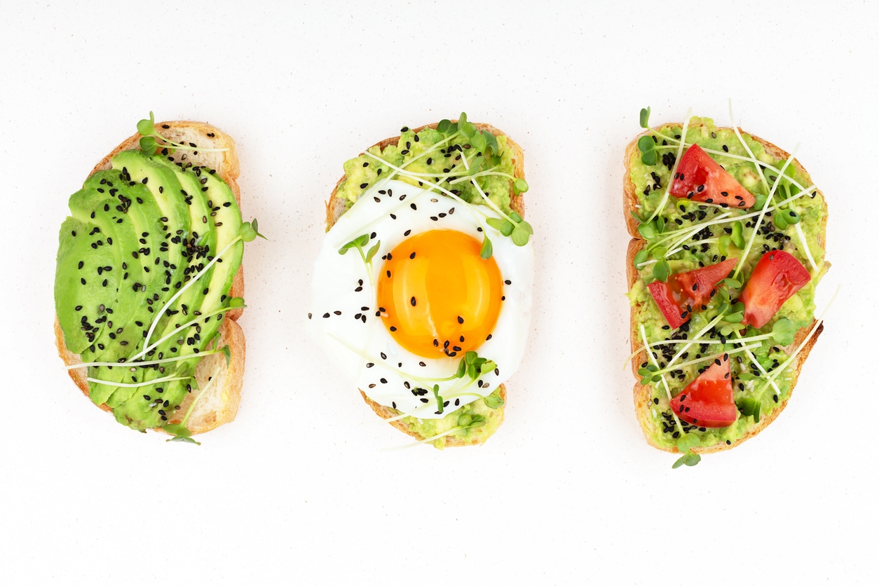 Three healthy toasts with egg, avocado, micro greens and tomatoes.